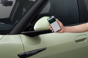 Nahaufnahme einer Hand, die ein Smartphone mit digitalem Fahrzeugschlüssel vor den Seitenspiegel hält.