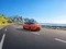Oranger Kleinwagen vor Meer/Bergsilhouette