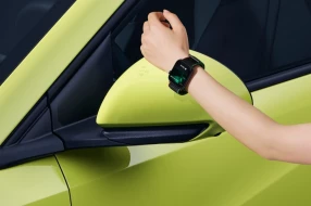 Person hält Smartwatch an einen neongelben Außenspiegel eines Autos zur kontaktlosen Fahrzeugöffnung via NFC-Technologie.