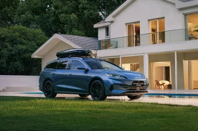 Blauer BYD SEAL 6 DM-i Touring mit Dachbox in frontaler Seitenansicht vor einem Haus geparkt.