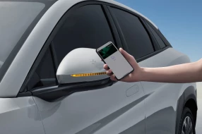 Eine Hand hält ein Smartphone mit NFC-Schlüssel an den Außenspiegel der Fahrertür, um das Fahrzeug zu entsperren.