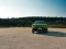 Grüner Jeep Compass in Frontansicht auf einer Schotterstraße vor mediterraner Landschaft