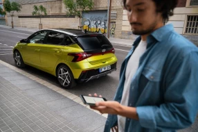 Ein neongrüner Hyundai Kleinwagen in Heckansicht geparkt am Straßenrand, im Vordergrund ein Mann.