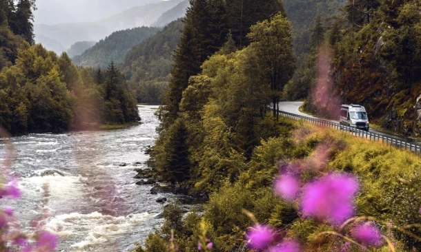 Wohnmobil fährt auf einer kurvigen Straße, entlang eines Flusses in den Bergen.