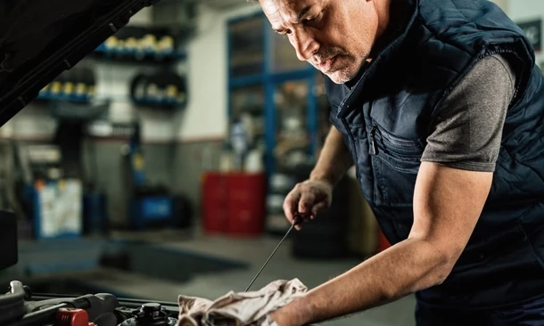 Mechaniker prüft Ölstand im Motorraum, hält einen Ölmessstab in der Hand und wischt ihn mit einem Tuch ab.