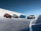 Vier moderne Autos in verschiedenen Farben auf geschwungener Betonfläche unter blauem Himmel.