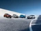 Vier moderne Autos in verschiedenen Farben auf geschwungener Betonfläche unter blauem Himmel.