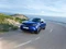 Blauer Opel Mokka auf einer Landstraße vor dem Meer.