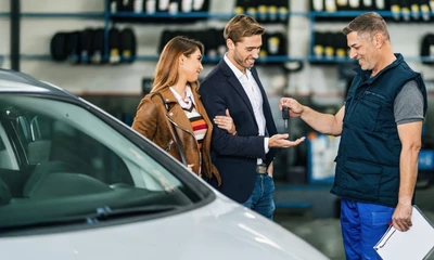 Kummich Mechatroniker überreicht einem zufriedenen Kunden-Paar den Autoschlüssel in der Werkstatt.