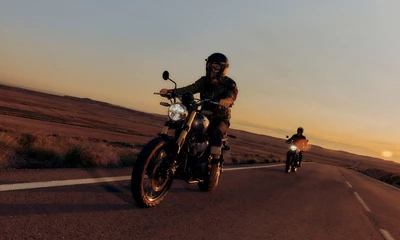 Royal Enfield Bear fahrend auf einer Straße in der Dämmerung, dahinter noch ein Motorrad.