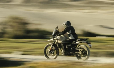Eine Himalayan 450, die mit Tempo eine Landstraße hinunterfährt. Seitliche Aufnahme.