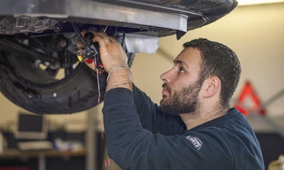 Kummich Mitarbeiter arbeitet konzentriert am Unterboden eines Fahrzeugs.
