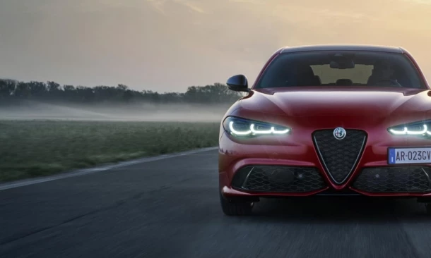 Ein glänzend roter Sportwagen fährt auf einer asphaltierten Straße. Leuchtende LED-Tagfahrlichter zieren die Front des Alfa Romeo.
