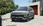 Ein hellgraues Elektro-SUV mit futuristischem Design parkt auf einer gepflasterten Einfahrt vor einem modernen Haus.