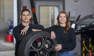 Ein Mann und eine Frau stehen in Werkstatt vor einem Reifen mit Felge.