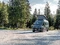Graues Crosscamp Freizeitmobil parkt auf Schotterparkplatz im Wald, umgeben von Bäumen und Natur.