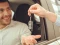 Männlicher Fahrer im Auto streckt Hand aus, eine zweite Hand übergibt ihm einen Autoschlüssel.