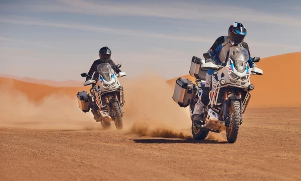 Zwei Honda Africa Twin Adventure Sports Motorräder fahren schnel durch die Wüste.