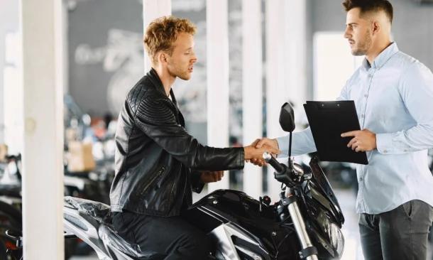 Ein Verkäufer schüttelt dem Kunden die Hand, der auf einem Motorrad sitzt.