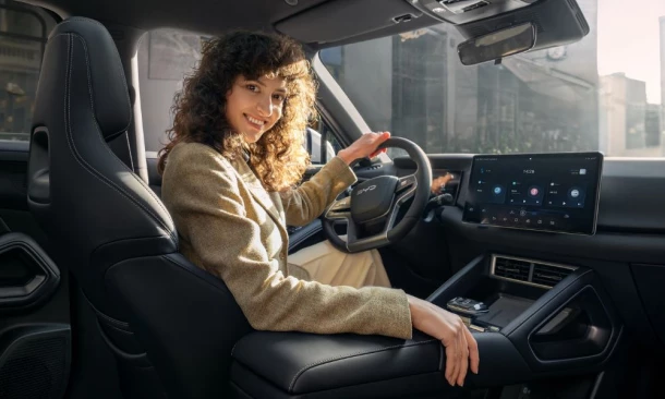 Frau sitzt im BYD E-Fahrzeug am Steuer und lächelt über die Schulter nach hinten.