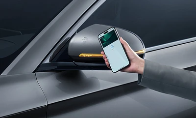 Graues Elektroauto – Nahaufnahme des Seitenspiegels, Smartphone wird per NFC zur Fahrzeugöffnung genutzt.