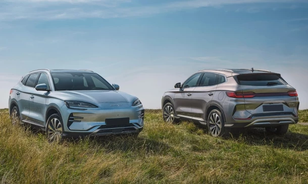 Zwei moderne Elektro-SUVs stehen auf einer grünen Wiese unter einem blauen Himmel mit einigen Wolken.