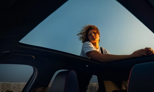 Person lehnt sich von außen an das offene Schiebedach eines Autos und genießt den Sonnenuntergang.