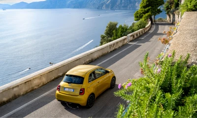 Gelber Fiat 500 vor einem Meerespanorama auf einer Straße, Blick von oben-seitlich.
