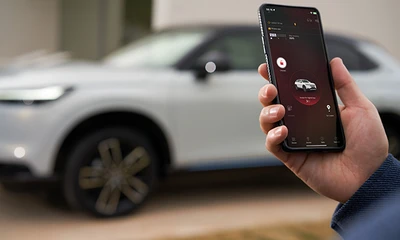 Hand hält Handy, im Hintergrund ein verschwommenes Auto.