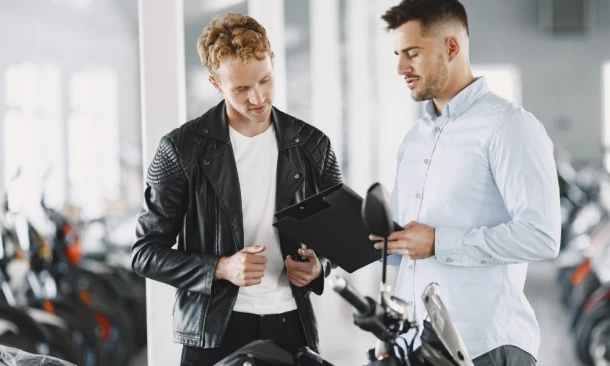 Zwei Männer stehen an einem Motorrad und unterhalten sich locker über ein Schriftstück.