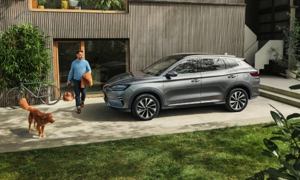 Ein Mann läuft mit seinem Hund um seinen City-SUV, im Hintergund ist ein modernes Haus in Grünen.