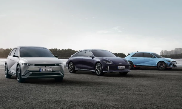 Drei Hyundai der IONIQ Reihe parken auf einem Kiesboden vor einer urbanen Landschaft mit einem Fluss.