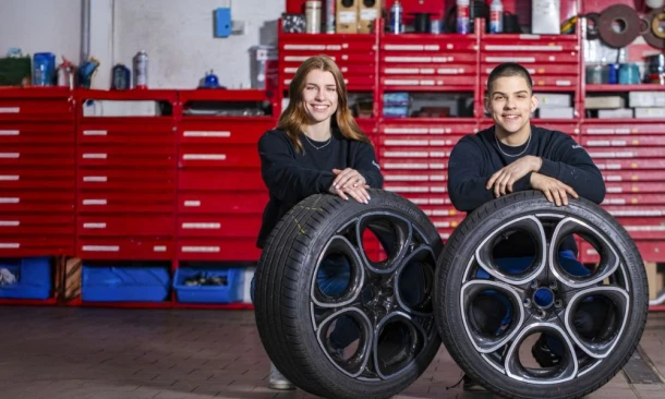 Zwei Mitarbeiter der Kummich Fahrzeugwelt hocken vor zwei Autoreifen mit Leicht-Metall-Felgen in der Werkstatt.