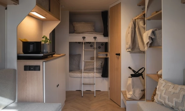 Modernes Camper-Interieur mit Etagenbetten, kleiner Küche und Stauraum.