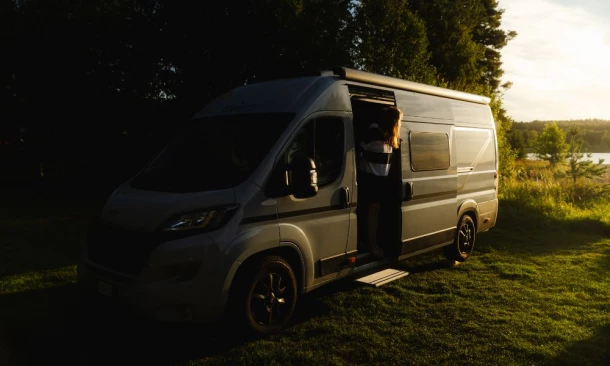Ein Wohnmobil parkt bei Sonnenuntergang auf einer grasbewachsenen Fläche am Rande eines Seeufers.