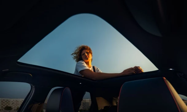 Perspektive durch das offene Autodach auf eine Frau die gegen das Auto lehnt.