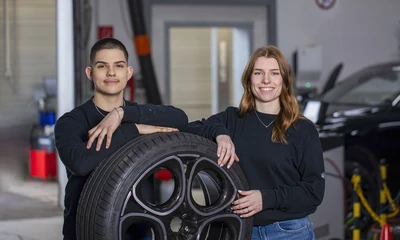 Ein Mann und eine Frau stehen in Werkstatt vor einem Reifen mit Felge.