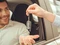 Männlicher Fahrer im Auto streckt Hand aus, eine zweite Hand übergibt ihm einen Autoschlüssel.