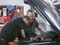 Zwei Kummich Werkstatt-Mitarbeiter arbeiten enthusiastsisch am Motor eines PKWs.