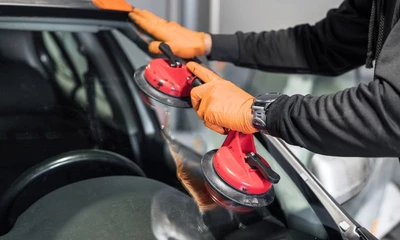 Eine Fahrzeugscheibe wird mit einem Sauggriff von einem Werkstatt-Mitarbeiter neu eingesetzt.