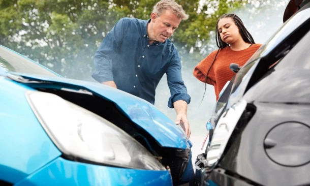 Eine Frau und ein Mann stehen genervt und erstaunt an der Unfallstelle ihrer Autos. Der Unfall wurde durch einen Anfahrt-Unfall verursacht.