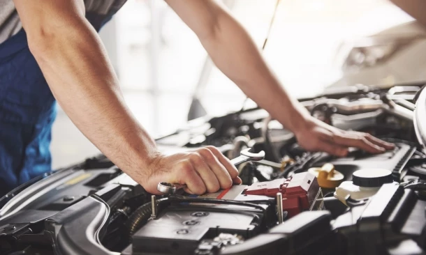 Automechaniker arbeitet in der Garage am Auot bei offener Motorhaube.
