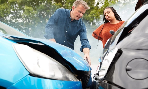 Eine Frau und ein Mann stehen genervt und erstaunt an der Unfallstelle ihrer Autos. Der Unfall wurde durch einen Anfahrt-Unfall verursacht.